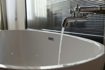 Close up shot of a vintage two handle faucet with running water in a bathroom. Chrome retro styled water mixer filling the bathtub. Copy space, background.