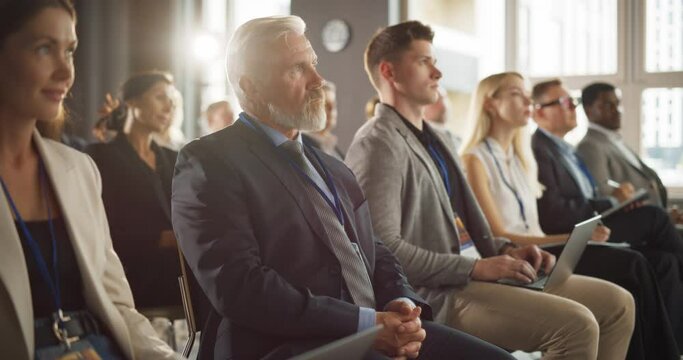 Senior Caucasian Male Entrepreneur Sitting In Diverse Crowd On Business Forum. Successful Investor Listening To Presenter Pitching Startup Idea On Stage. Businessman Attending Technology Conference.
