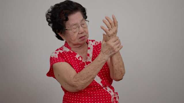 Elderly Asian woman patients suffer from numbing pain in hands from rheumatoid arthritis. Senior woman massage her hand with wrist pain. Concept of joint pain, rheumatoid arthritis, and hand problems.