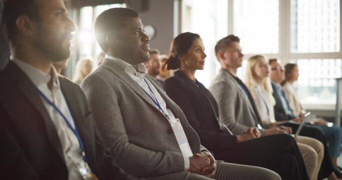 African Man Sitting in Crowded Auditorium at a Tech Conference. Professional Businessman Listening To Keynote. Specialist Watching Innovative Technology Presentation About New Software Solutions.