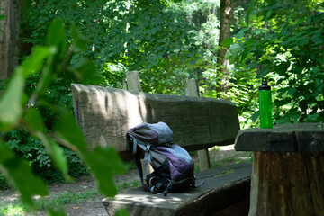 Hiking backpack on wooden bench in the forest, green water bottle with water - 653268249