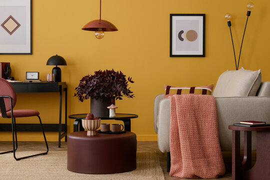 Cozy living room interior with mock up poster frame, yellow wall, burgund coffee table, pink plaid, beige sofa, bleck desk, lamp and personal accessories. Home decor. Template.