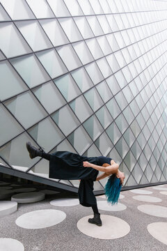 Flexible young dancer bending over backwards in front of modern building