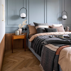 Interior design of cozy bedroom with brown and grey bedding, pillows, bedside table, vase with...
