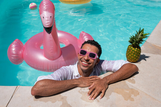 Happy man leaning with pineapple and inflatable swimming ring by poolside