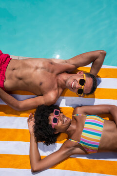 Happy friends lying on stripped towel with eyes closed near pool