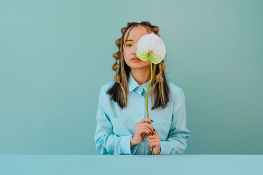 Naklejki Young woman covering eye with flower against blue background