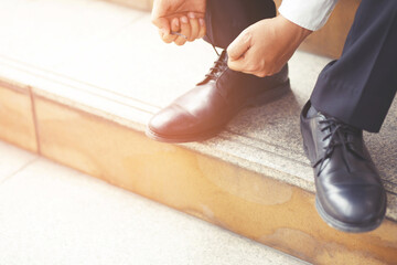 Close up of businessman hand tie shoelaces wearing leather shoes sitting on staircase background.