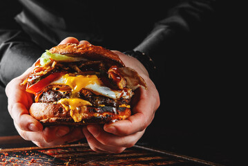 Man's hands holding burger with meat, cheese and vegetables - obrazy, fototapety, plakaty