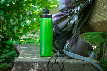  Hiking backpack on wooden bench in the forest, green water bottle with water - 653278008
