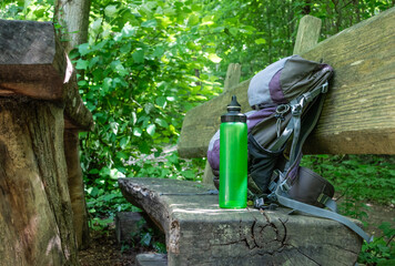  Hiking backpack on wooden bench in the forest, green water bottle with water - 653278010