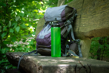  Hiking backpack on wooden bench in the forest, green water bottle with water - 653278012