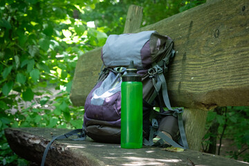  Hiking backpack on wooden bench in the forest, green water bottle with water