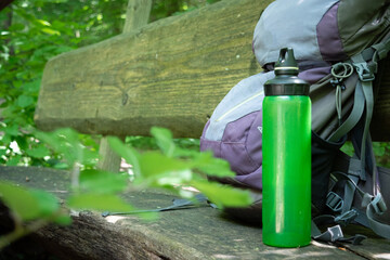  Hiking backpack on wooden bench in the forest, green water bottle with water - 653278043