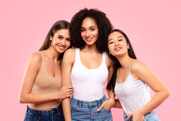 Fototapeta premium Happy young asian, black and european women posing and enjoying their natural beauty, standing on pink background