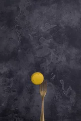 Poster Yellow macaron on a golden fork isolated on black background.  © Evis