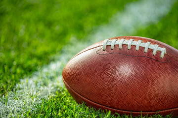A low angle close-up view of a leather American Football sitting in the grass next to a white yard line.