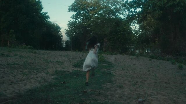 A frightened girl in a bloodstained dress runs away from her pursuer through the woods