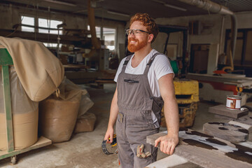 Professional woodworker in eyeglasses standing on the background on carpentry workshop