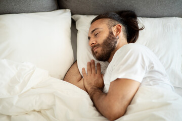 Top view of sleeping bearded young man lying in bed