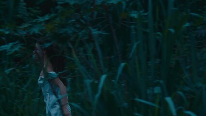 A frightened girl in a bloodstained dress runs away from her pursuer through the woods