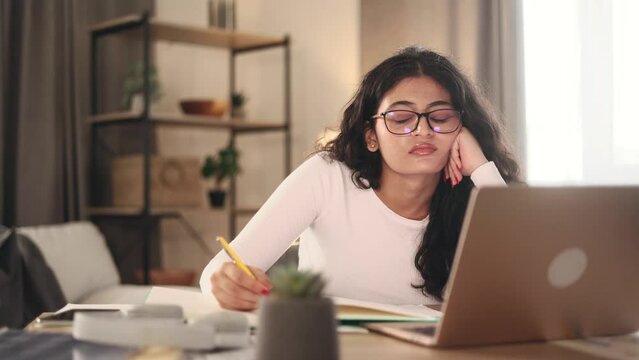 Boring tired young student freelancer with glasses can not study or work making notes at home workplace Stressed curly female exhausted from remote distance work or education and hard program indoors