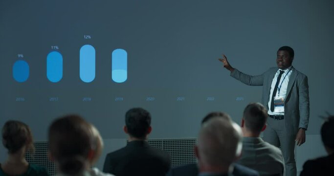 Corporate Event: Black Male Marketing Director Giving Presentation To Colleagues or Investors In Conference Room Of Innovative Startup Office. African Man Talking About Advertising Channels, Budget.