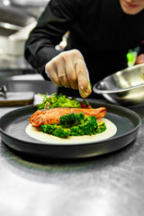 chef hand cooking salmon steak with broccoli and sauce on restaurant kitchen