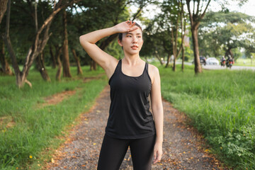 Young Asian woman wiping away sweat after jogging at the park.