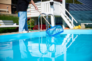 Young woman cleans swimming pool. Personnel cleaning the pool from leaves in sunny summer day. Hotel staff worker cleaning the pool. Cleaning swimming pool service. Purification with a net.