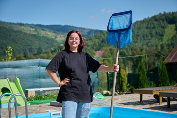 Enthusiastic cleaner ready to work. Young female holding cleaning equipment for swimming pools....