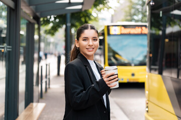 Beautiful young multiracial hispanic business woman using public transportation in city smiling and holding eco thermo cup with coffee