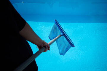 Young woman cleans swimming pool. Personnel cleaning the pool from leaves in sunny summer day. Hotel staff worker cleaning the pool. Cleaning swimming pool service. Purification with a net. Close up