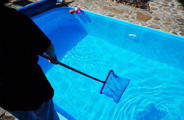 Young woman cleans swimming pool. Personnel cleaning the pool from leaves in sunny summer day. Hotel staff worker cleaning the pool. Cleaning swimming pool service. Purification with a net. Close up