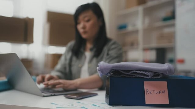 Asian female small business owner processing returned orders, checking clothing
