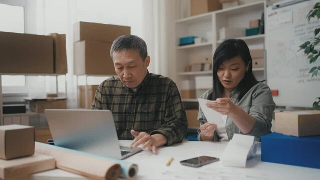 Middle-aged Asian woman and her father doing taxes in office, family business