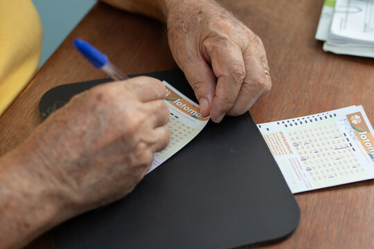 Close nas m&atilde;os de um homem idoso que est&aacute; a marcar os n&uacute;meros em uma cartela de jogo de loteria.