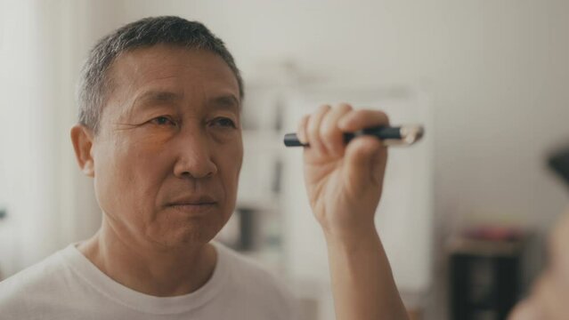 Doctor checking pupillary reflex of senior Asian man using flashlight, neurology