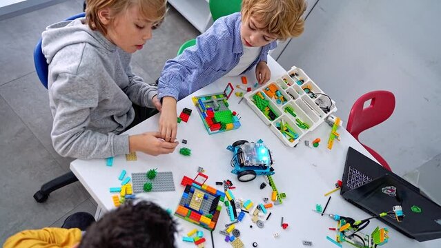 Robotics programming class. Children construct and code Robot. STEM education using constructor blocks and laptop tablet, remote control joystick. Technology educational development for school kids