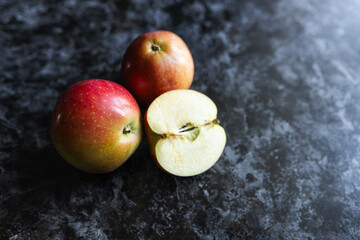 Red apples, cut into halves, lie on a  a dark background. Apple slices on a marble table close-up. Fruits on a gray background