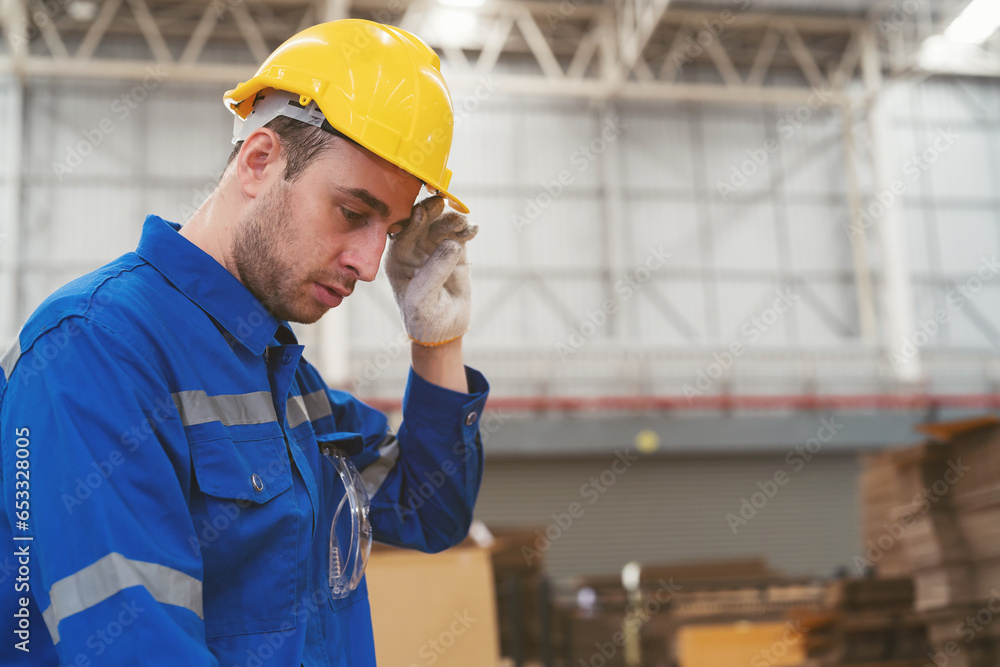 Wall mural Tired male engineer worker working in factory in break time. Male worker working and wearing safety uniform, helmet in industry factory