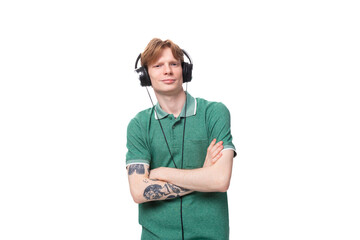 young IT specialist red-haired men in a green t-shirt listens to music in wired headphones during a break at work