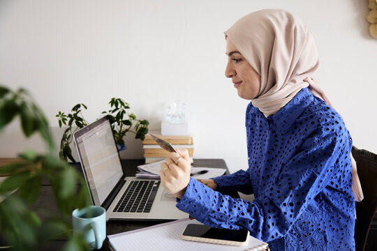 Woman in headscarf paying bills online at home