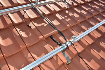 Dachdecker beim Aufbau einer Photovoltaikanlage auf einem neu gedeckten Ziegeldach: Befestigung der...