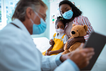 Senior pediatrician entertaining his young patient with a tablet in a medical office