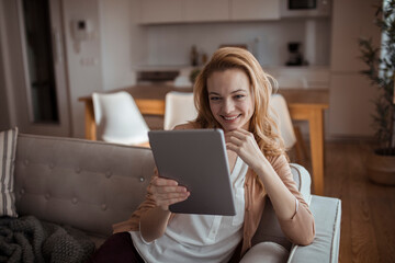 Young redhead woman using the tablet on the couch at home