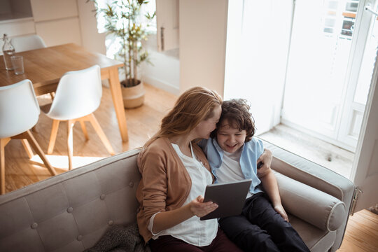 Young mother using the tablet with her son on the couch at home