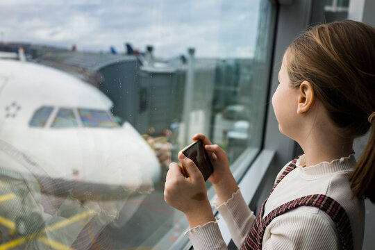 Young girl taking a picture on her smartphone of a airplane at the airport