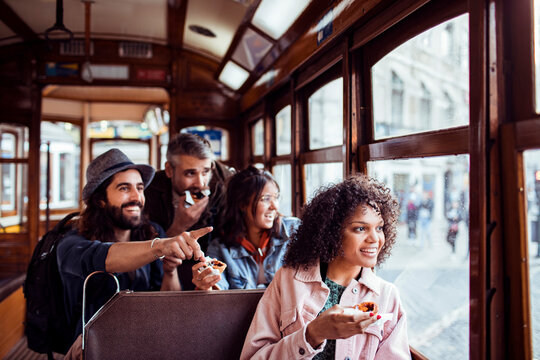Young and diverse group of friends having a snack on a tram and sightseeing through the windows
