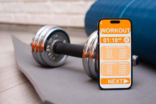  monitoring physical activity app next to an exercise mat, dumbbell and roller. Practicing sports, keeping fit and healthy.